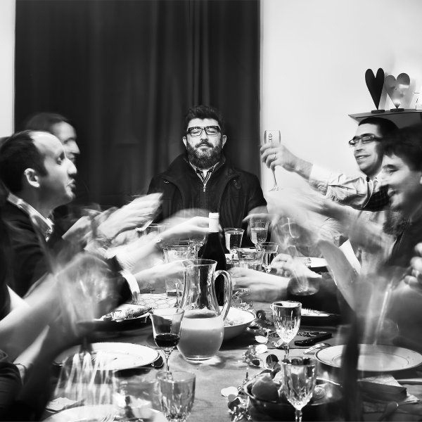 Des gens réunis autours d'un repas de fête célèbre alors qu'un homme en bout de table a le visage fermé